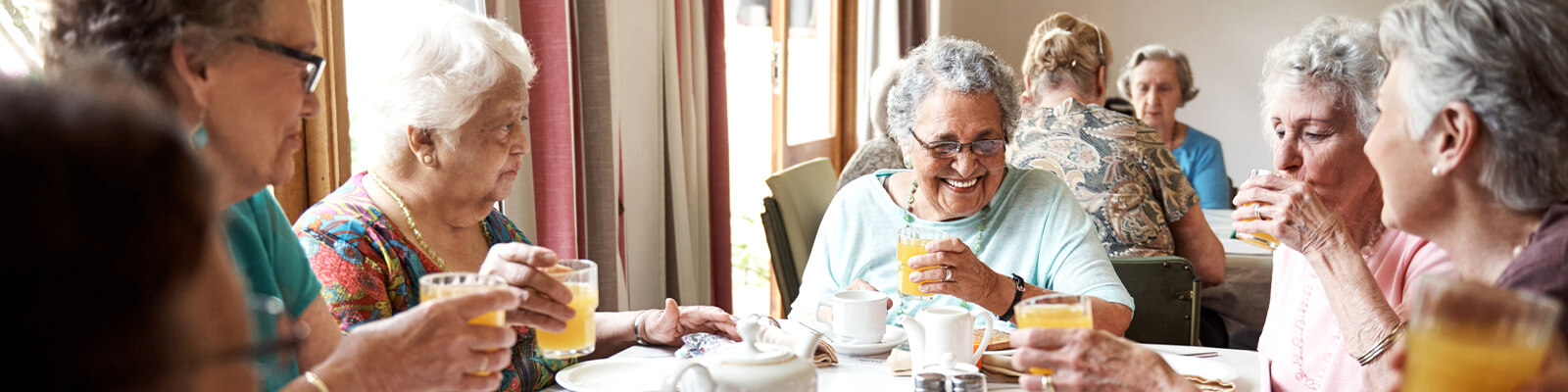 A group of female senior living residents sitting at a table drinking orange juice and eating breakfast