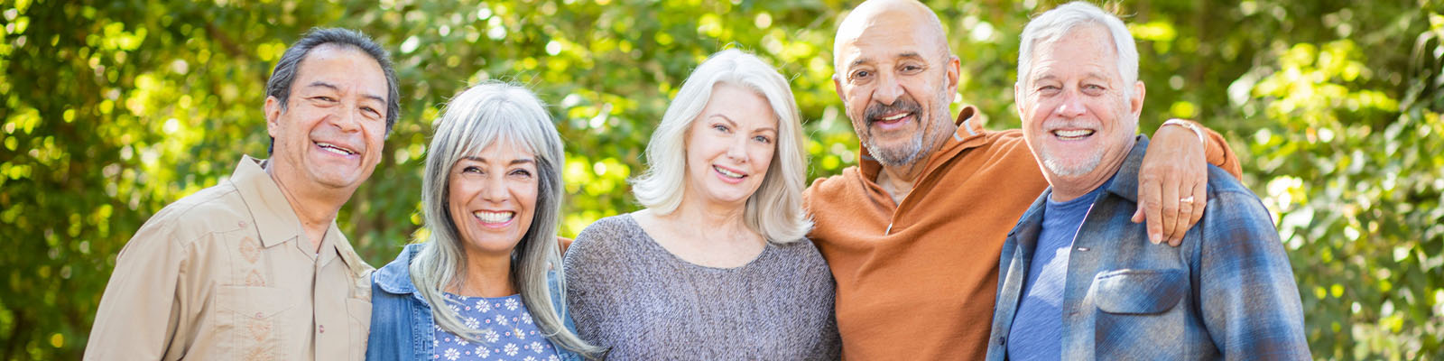 A group of senior men and senior women standing together outdoors in a park with their arms around each other's shoulders